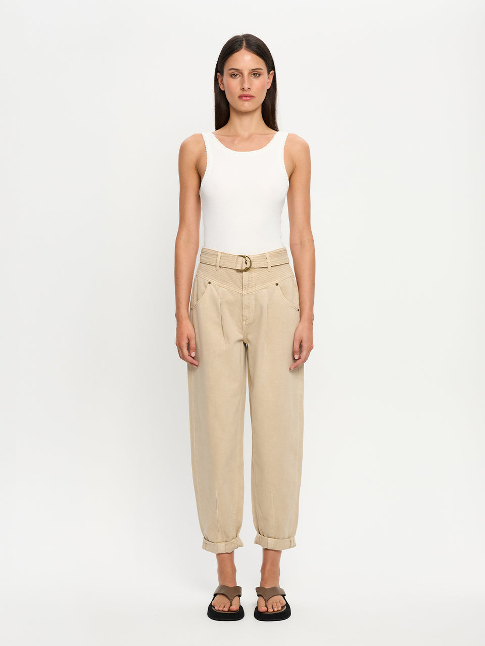 Woman wearing a white tank top and beige denim jeans on a white background