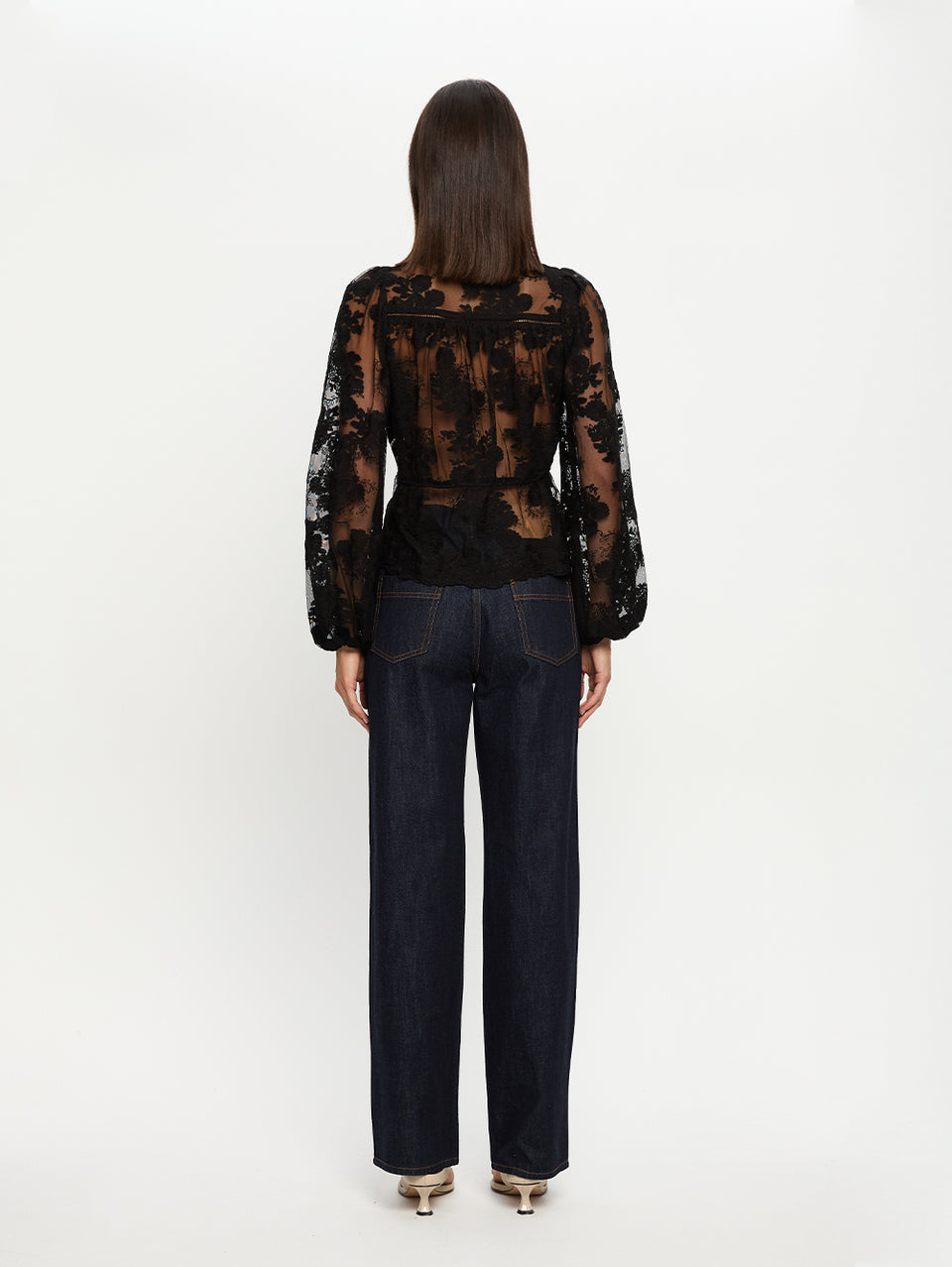 Person wearing a black lace top and dark jeans on a white background