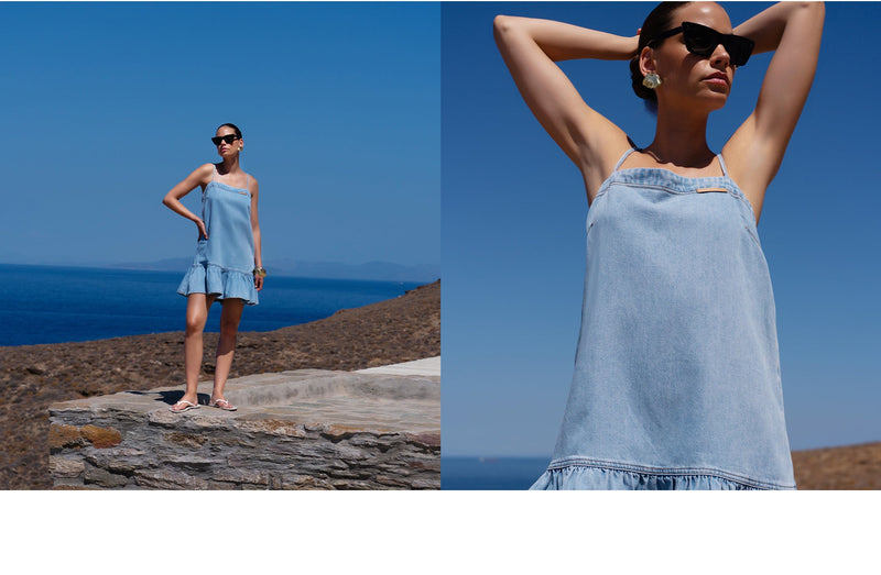Woman in a light blue dress standing on a rocky cliff with ocean view.