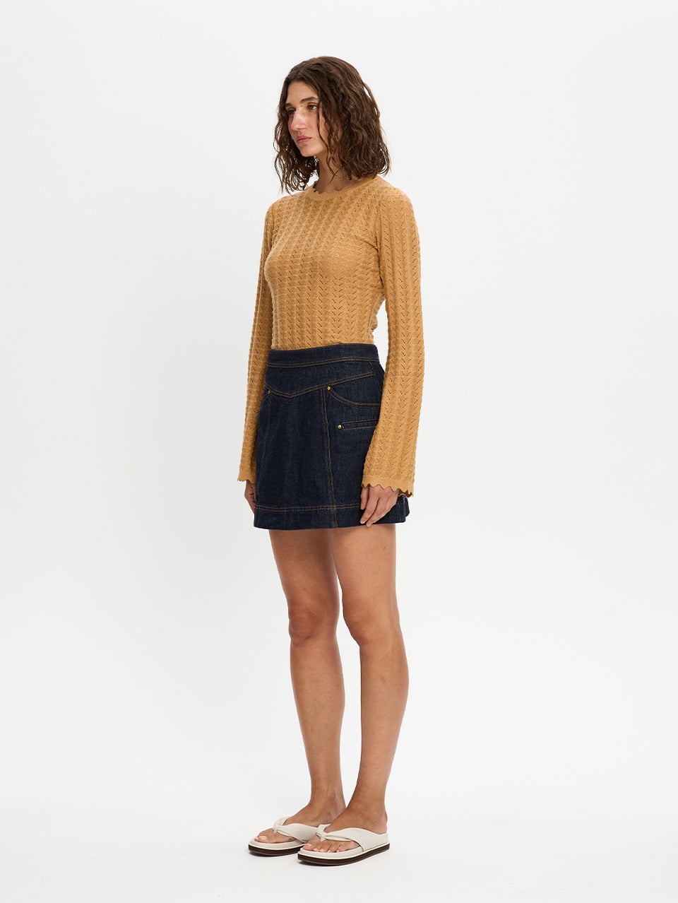 Woman wearing a mustard yellow sweater and dark denim skirt on a white background