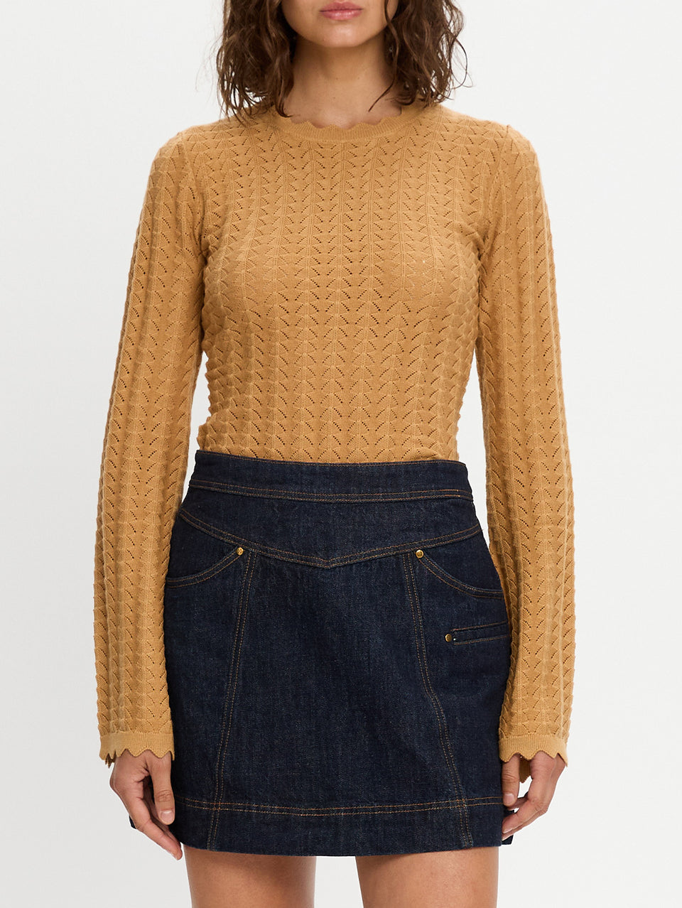 Person wearing a mustard yellow cable knit sweater and dark blue denim skirt on a white background